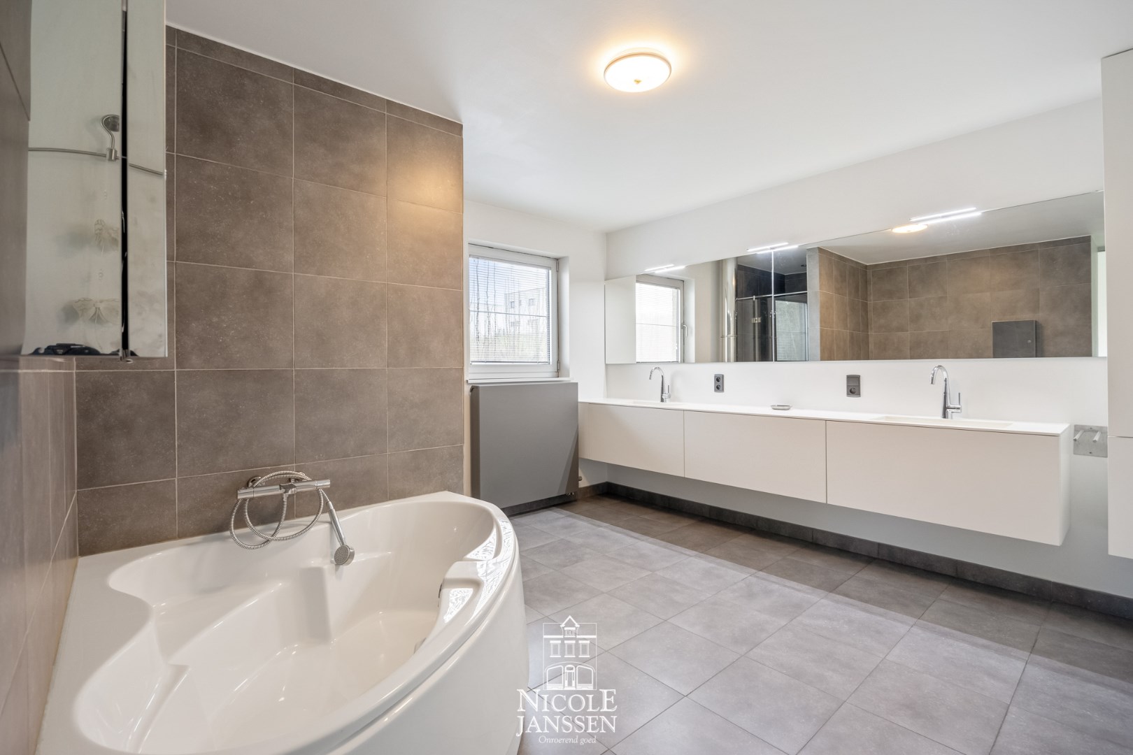 Ensuite badkamer met hoekbad, douche en dubbele lavabo in fraai badkamermeubel 